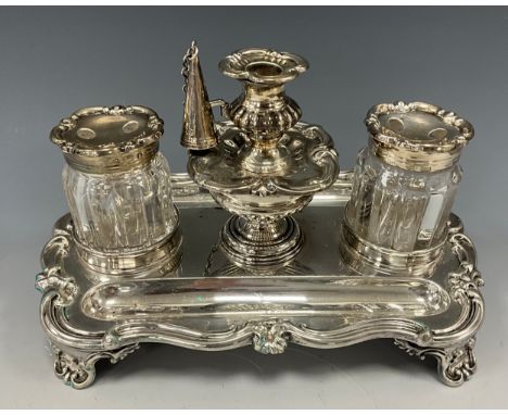 A George IV silver inkstand, shaped rectangular scrolling base, with two pen rests, two glass silver topped pounce pots/inkwe