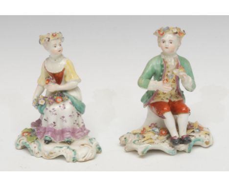 A pair of Derby patch mark figures, of a boy and girl, both seated, wearing floral chaplets, holding flower posies, decorated