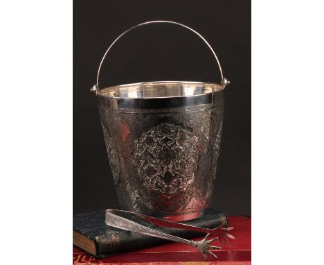 An Iranian silver ice bucket, profusely chased in the Persian taste, tongs en suite, 18.5cm high excluding swing handle, mark