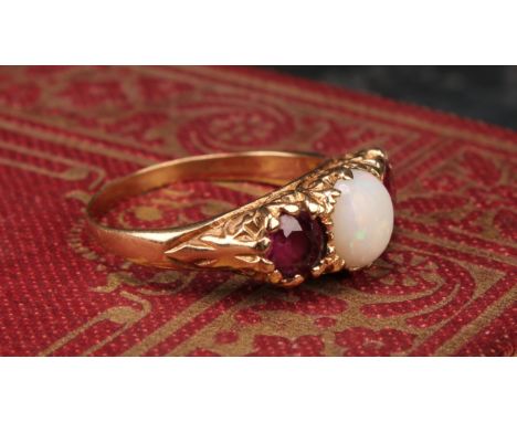 An opal and ruby ring, central cabochon opal flashing green, blue, red and orange play, mounted between oval pale pinky red r