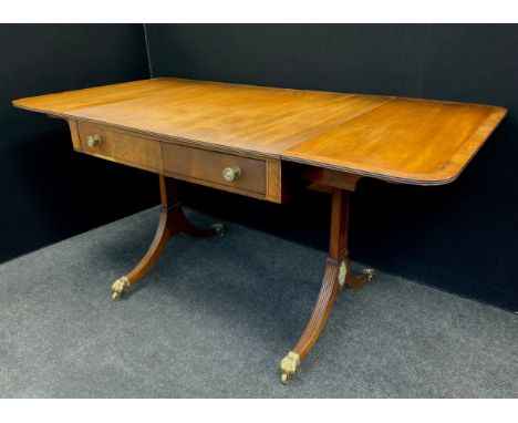 A Regency mahogany sofa table, the rounded rectangular drop-leaf top with a pair of drawers to each frieze, reeded sabre legs
