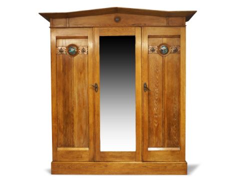 An Arts and Crafts oak triple wardrobe manufactured by Lebus, Louis & Harris, c.1905, The arched cornice above central mirror