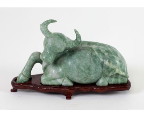 A small carved Jade? figure of a Buffalo Resting, on a wooden stand, 11.5cms x 20.5cms (4 1/2" x 8"). (1)