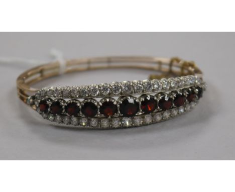 A Victorian style yellow metal, garnet and white sapphire? set hinged bangle.