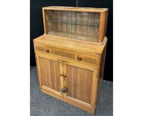 A 20th century light oak Priory style side cabinet, two door glazed top above frieze drawer and pair of panelled cupboard doo