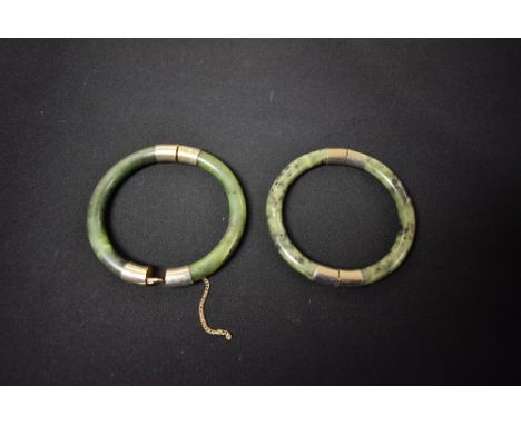 A metal mounted polished green and black spotted hardstone bangle, possibly jadite, white metal mounts; another similar (2)