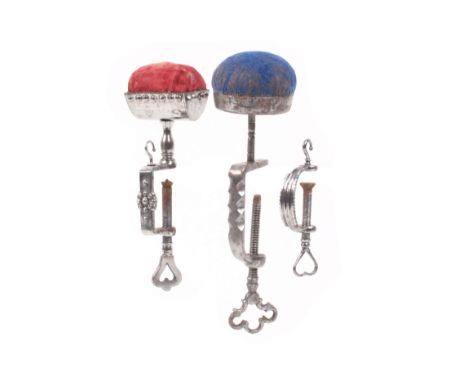 Three polished steel sewing clamps, comprising a cut steel example with hook below a trough form pincushion top, 14cm, anothe