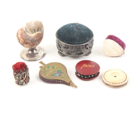 Seven pincushions comprising a natural shell form example on silver base, Birmingham 1909, 5.2cm, a circular Chinese example 