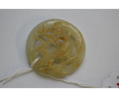 A Chinese pale carved and pierced celadon jade roundel, decorated with birds in flowering branches, with russet coloured high