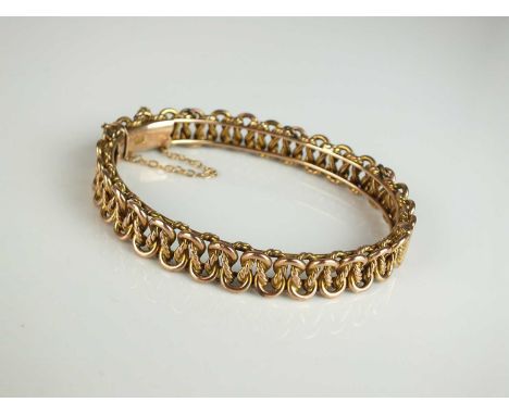 A late 19th / early 20th century entwined scroll link openwork bangle, with integral clasp stamped '9ct' and attached safety 