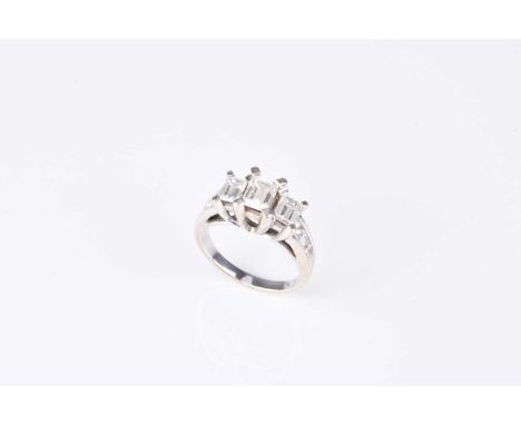 A graduated emerald cut three stone diamond ring, the three emerald cut diamonds claw set in white metal to graduated Princes
