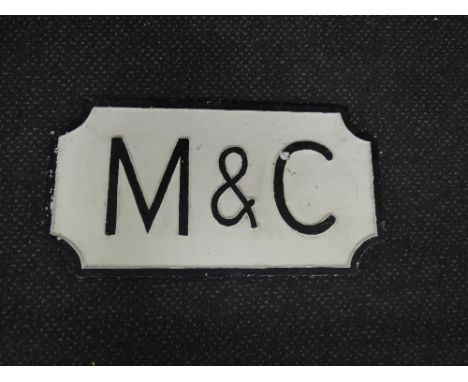 A cast sign, M & C, white background, black letter and border
