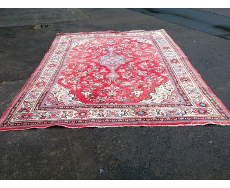 An Iranian carpet woven with red floral Paisley style panel to rectangular field, bordered by a frieze of linked flower heads