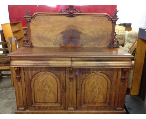 A Victorian mahaogany sideboard, the back with panel in moulded frame having applied scrolled carvings, the base with two cus