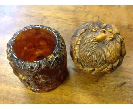 A carved hardwood ball netsuke entwined with horned rams having inlaid bead eyes; and an amber ring moulded with stylised bea