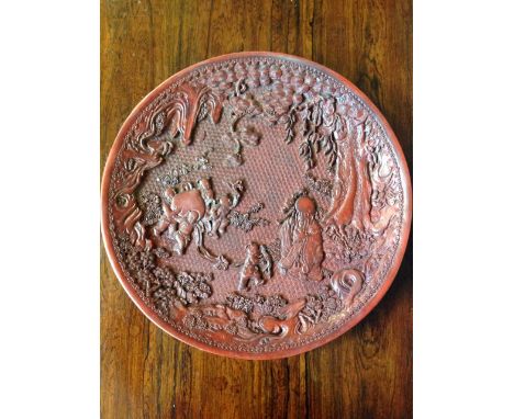 A cinnabar lacquer dish decorated with children and an ancient playing in a garden on honeycomb ground framed by foilage, tre