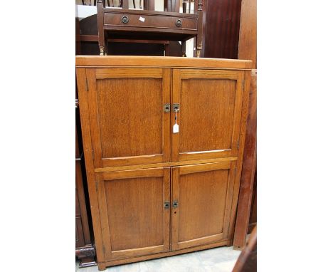 An early 20th Century oak two-tier cupboard, the upper and lower sections both fitted with two panelled doors enclosing a sin