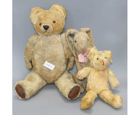 A gold plush teddy bear with plastic eyes, black stitched snout and worn brown leather pads, height 56cm, a smaller later bea