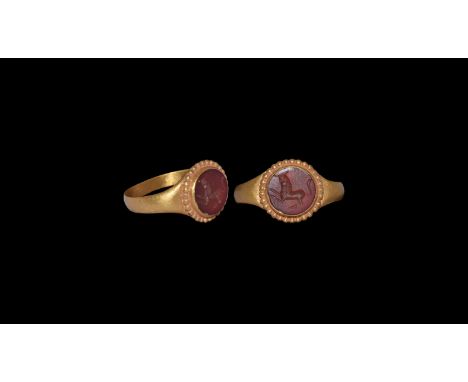 An undated archaistic gold finger ring comprising a flat-section hoop and discoid plaque with beaded border, with carnelian i