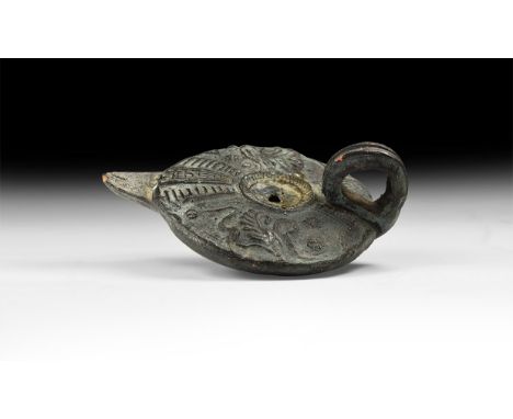 An undated archaistic ceramic oil lamp, discoid in plan, biconvex with loop handle, short nozzle, raised geometric detailing 