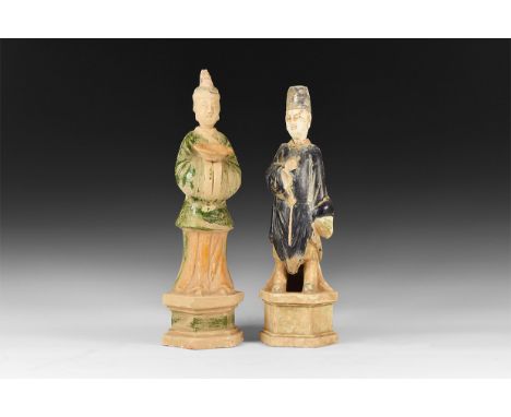 An undated archaistic pair of ceramic statuettes of male attendants wearing caps, tunics and boots, heads separate; one holdi