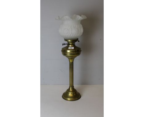 A brass column oil lamp, having a moulded and frosted glass shade over the burner with twin adjusters and brass reservoir, th