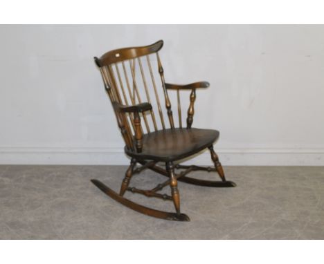 A stained wood rocking chair in the style or Ercol, with spindle supports and shaped arms 84cm high