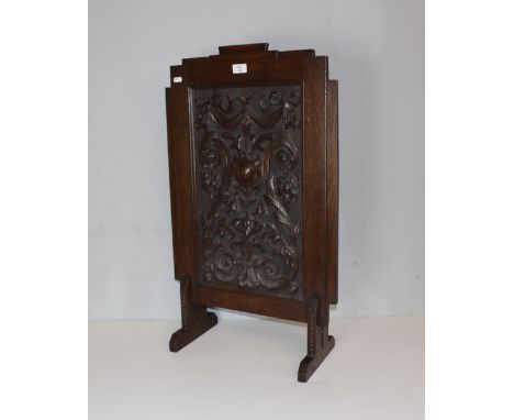 A carved oak firescreen, the rectangular panel carved in relief and stippled with ornate foliate scrolls, within a stepped fr