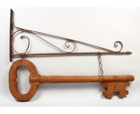 AN UNUSUAL FOLK ART/SHOP SIGN, modelled as a carved and painted wood key, suspended from a wrought iron bracket. 37ins wide.