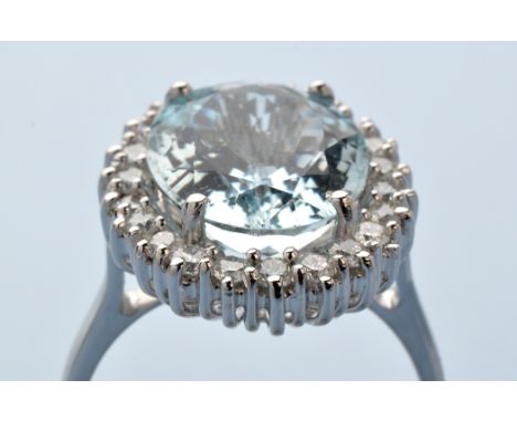An aquamarine and diamond cluster ring, the oval fact cut aquamarine surrounded by brilliant cut diamonds, on 18ct. white gol