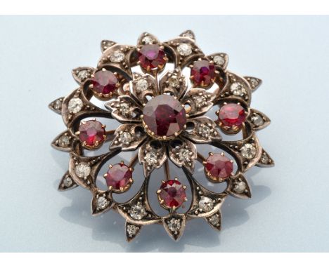 A diamond and ruby circular brooch of floral design, the central circular facet cut ruby in crown mount surrounded by eight d
