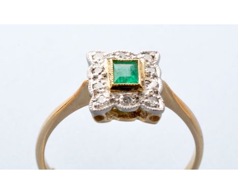 An emerald and diamond cluster ring, the rectangular facet cut emerald within yellow metal millegrain mount, surrounded by te