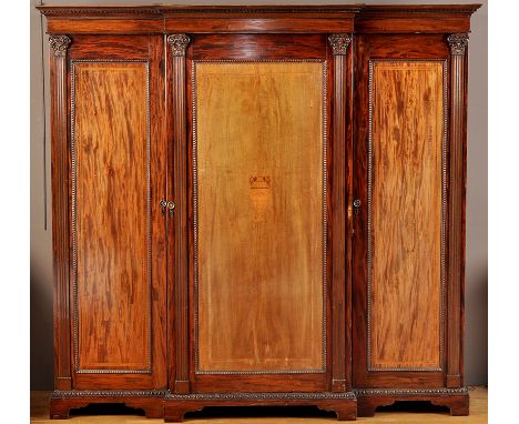 An early 20th Century mahogany breakfront wardrobe, the flared Greek key decorated cornice above central cupboard door inlaid