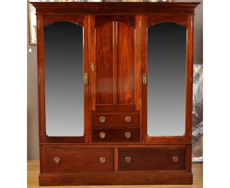 An early 20th Century mahogany wardrobe, the flared cornice above central arched panel door enclosing hanging space above two