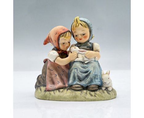 Features two small girls, one seated and one kneeling, as they gently pet a rabbit, while a second rabbit sits playfully besi