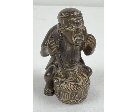 A small carved wood netsuke of an Oriental man stirring a barrel. Set with small mother of pearl disc to underside and with t