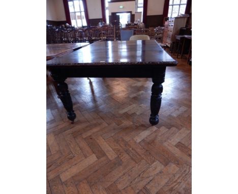 A Victorian ebonised oak wind-out dining table, with a foliate carved border, and two extra leaves, on turned carved bulbous 