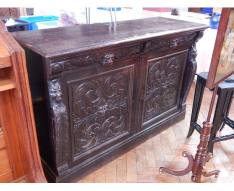 A Victorian stained oak cupboard with moulded edge top, the two frieze drawers with mask handles, pair of foliate carved pane