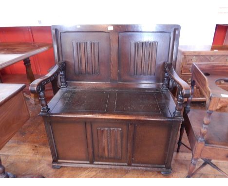 A stained oak monk's bench with linenfold panels, down swept arms to box base, on bun feet, width 100cm