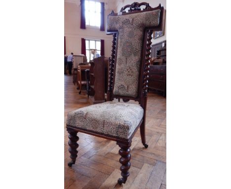 A Victorian walnut prie dieu chair with scroll carved crest rail, upholstered high back with turned spiral column supports, u