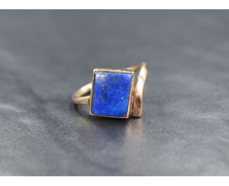 An Artisan style yellow metal ring stamped 9ct having a rectangular lapiz lazuli stone in a closed mount to offset shoulders,