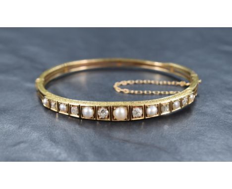 A hinged gold bangle having diamond and split pearl decoration to front panel, no marks but presumed gold, inner measurements
