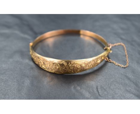 A 9ct gold hinged bangle, the tapered design having engraved floral and scroll decoration with a central 'C' initial, with sa