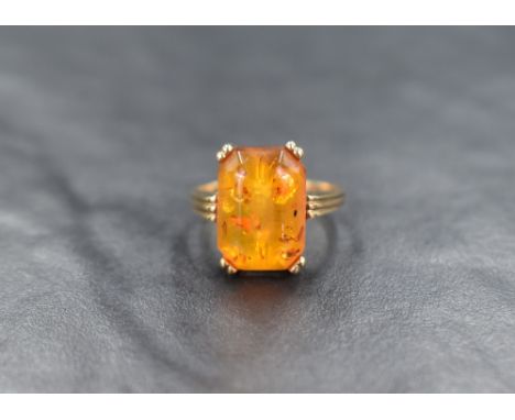 A 9ct gold Baltic amber ring, the shaped rectangular stone in a four claw set mount to reeded shoulders, ring size N and appr