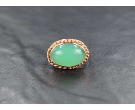 An oval jade style cabochon ring having a collared mount with twist wire decoration on a yellow metal loop, no marks but test