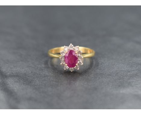 An 18ct gold ruby and diamond cluster ring having a small oval ruby surrounded by twelve small diamonds in a claw set mount, 