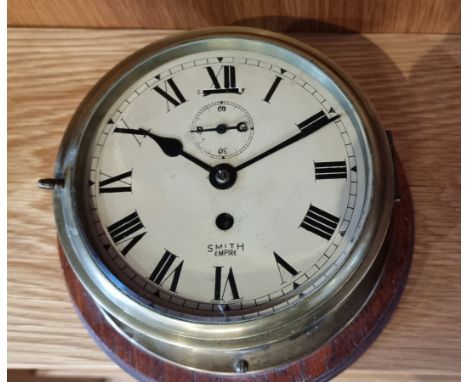 An early 20th century Smiths Empire brass cased bulkhead clock, having an 8 day movement, mounted on a mahogany backplate, 20