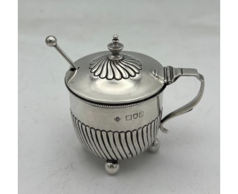 A simple “set-pot” shaped silver mustard pot with clear glass liner on four ball feet. The lower half of the body with slim w