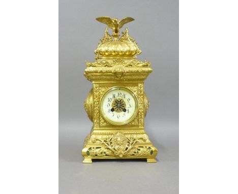 A late 19th century ornate brass mantel clock, with a spread eagle surmount, enamel dial and striking the hours and half hour