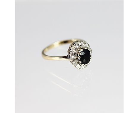 A sapphire and diamond oval cluster ring, the central sapphire within a surround of twelve diamonds, all set in white metal t